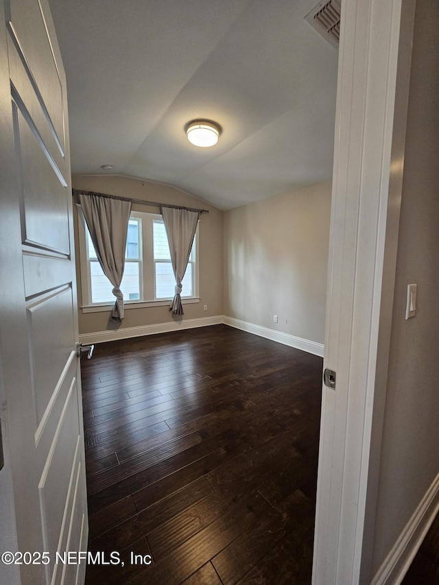 unfurnished room with baseboards, vaulted ceiling, and dark wood-type flooring