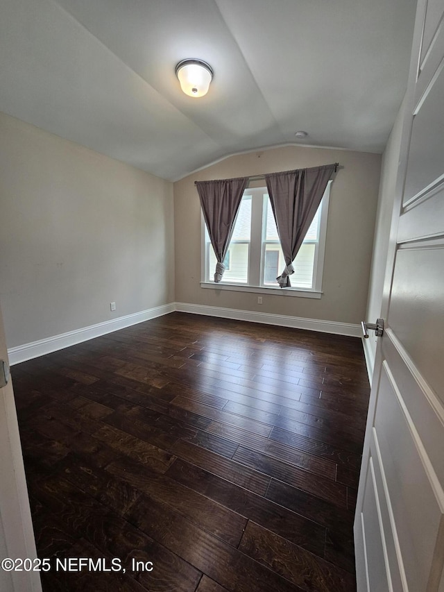 empty room with baseboards, vaulted ceiling, and dark wood-style flooring
