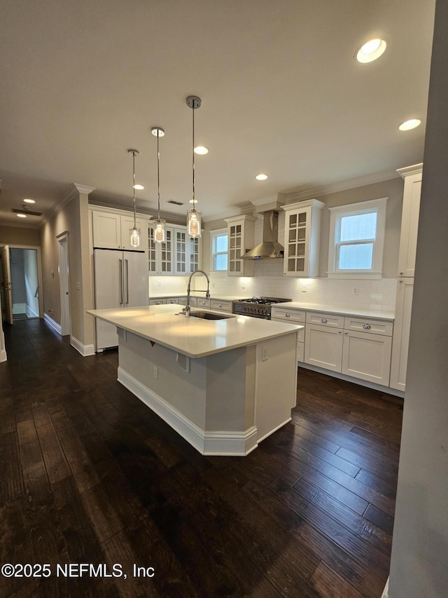 kitchen featuring wall chimney range hood, crown molding, a sink, tasteful backsplash, and premium appliances