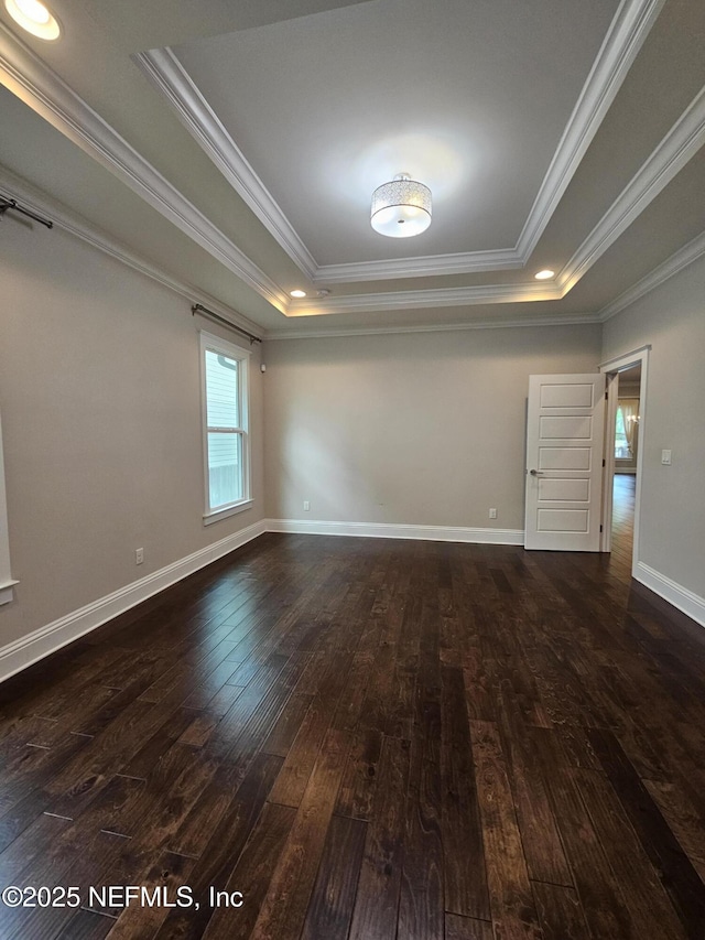 empty room with dark wood-type flooring, ornamental molding, a raised ceiling, and baseboards