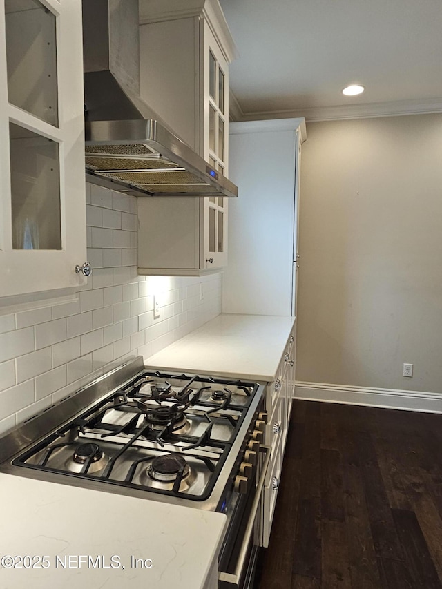 kitchen featuring wall chimney range hood, crown molding, stainless steel range with gas stovetop, baseboards, and glass insert cabinets