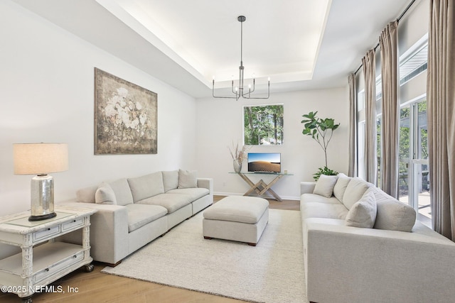 living area featuring a tray ceiling, wood finished floors, a chandelier, and baseboards
