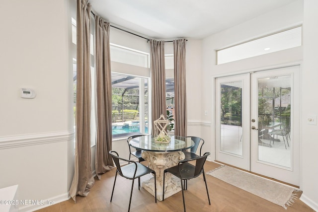 dining area with french doors, healthy amount of natural light, light wood-type flooring, and baseboards