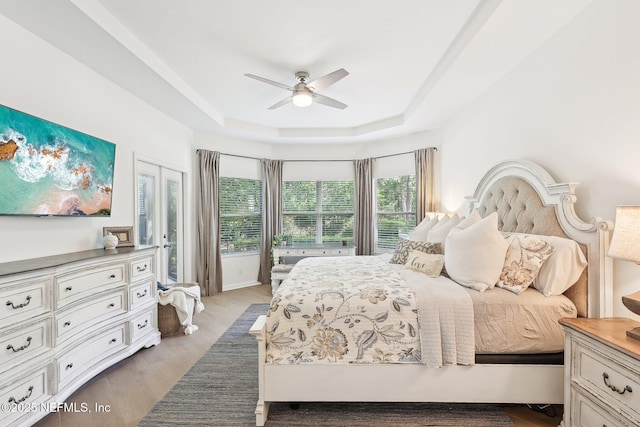 bedroom featuring a raised ceiling, wood finished floors, and a ceiling fan
