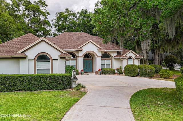 mediterranean / spanish-style house with stucco siding, roof with shingles, a front lawn, and driveway