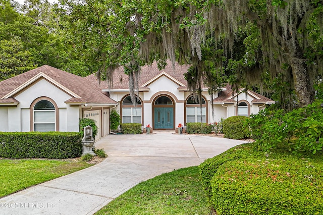 view of front of house with stucco siding, concrete driveway, roof with shingles, a garage, and a front yard