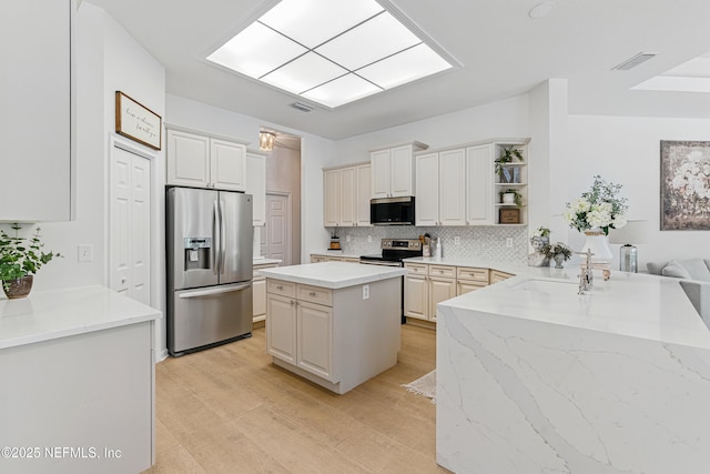 kitchen with appliances with stainless steel finishes, open shelves, light wood-type flooring, tasteful backsplash, and light stone countertops