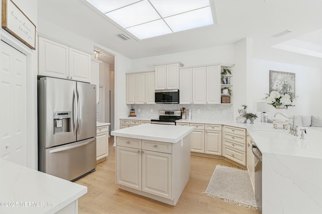 kitchen featuring appliances with stainless steel finishes, a sink, tasteful backsplash, light wood-type flooring, and a center island