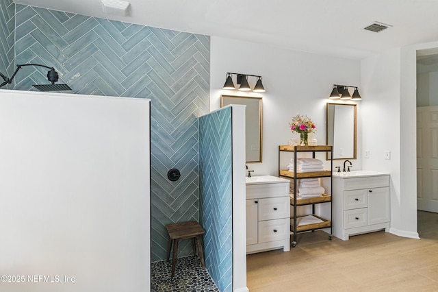 bathroom featuring two vanities, a walk in shower, and wood finished floors