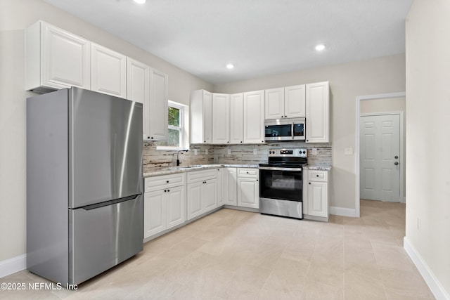 kitchen featuring light stone countertops, stainless steel appliances, tasteful backsplash, baseboards, and white cabinets