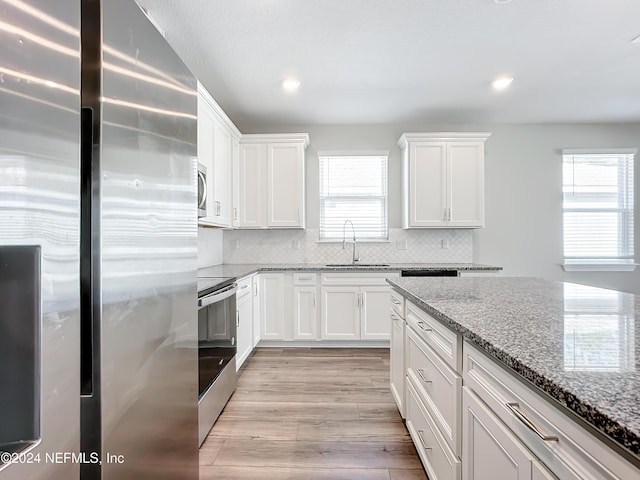 kitchen featuring light stone counters, white cabinets, light wood-style flooring, a sink, and stainless steel appliances