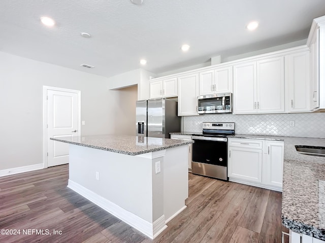 kitchen featuring tasteful backsplash, light wood-style flooring, appliances with stainless steel finishes, white cabinets, and a center island