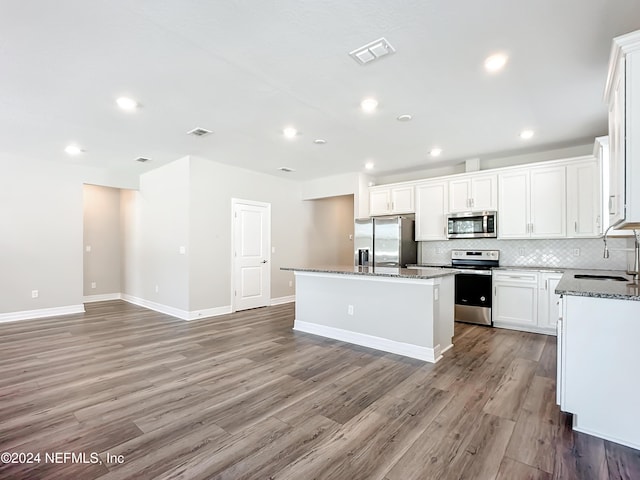 kitchen with a sink, decorative backsplash, light wood-style floors, a center island, and appliances with stainless steel finishes