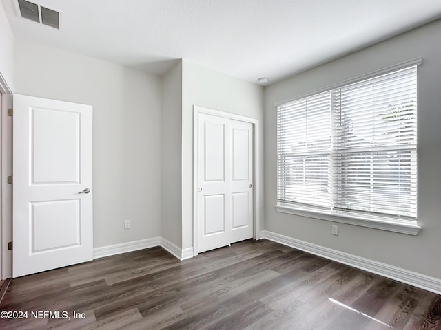 unfurnished bedroom with a closet, visible vents, baseboards, and dark wood-type flooring