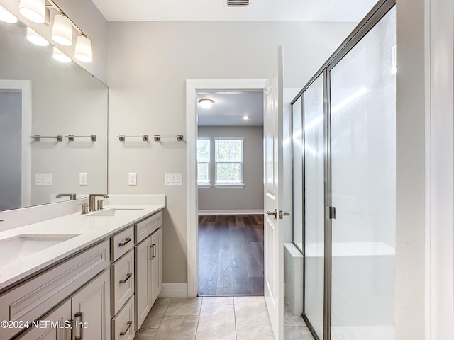 bathroom with baseboards, a stall shower, double vanity, and a sink
