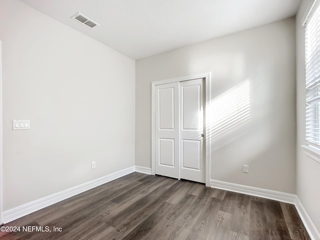 unfurnished bedroom featuring dark wood-style flooring, visible vents, a closet, and baseboards