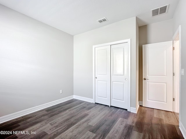 unfurnished bedroom with dark wood-type flooring, visible vents, and a closet