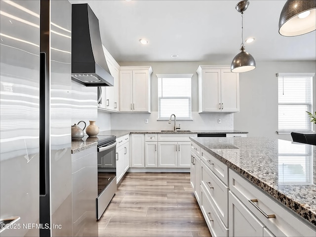 kitchen with wall chimney range hood, white cabinetry, a sink, stainless steel appliances, and light wood-type flooring