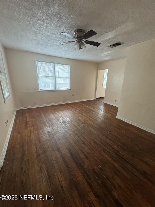 unfurnished room with visible vents, a textured ceiling, dark wood-style flooring, and plenty of natural light