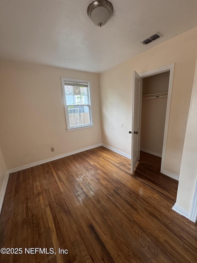 unfurnished bedroom with a closet, visible vents, dark wood-style flooring, and baseboards