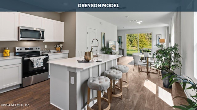 kitchen featuring dark wood-type flooring, white cabinetry, light countertops, an island with sink, and appliances with stainless steel finishes