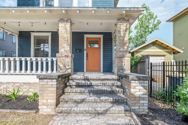 view of exterior entry featuring fence and covered porch