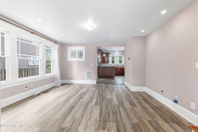 unfurnished living room featuring a healthy amount of sunlight, baseboards, light wood finished floors, and visible vents