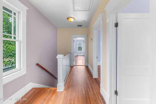 hallway featuring attic access, visible vents, light wood-type flooring, baseboards, and an upstairs landing