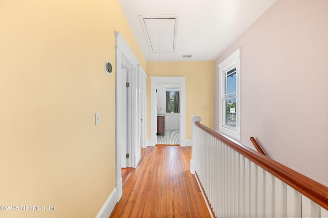 corridor featuring visible vents, baseboards, attic access, light wood finished floors, and an upstairs landing