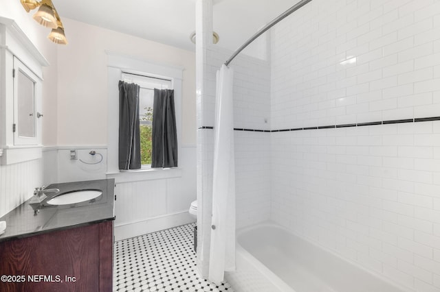 bathroom with vanity, shower / bathtub combination with curtain, wainscoting, and toilet