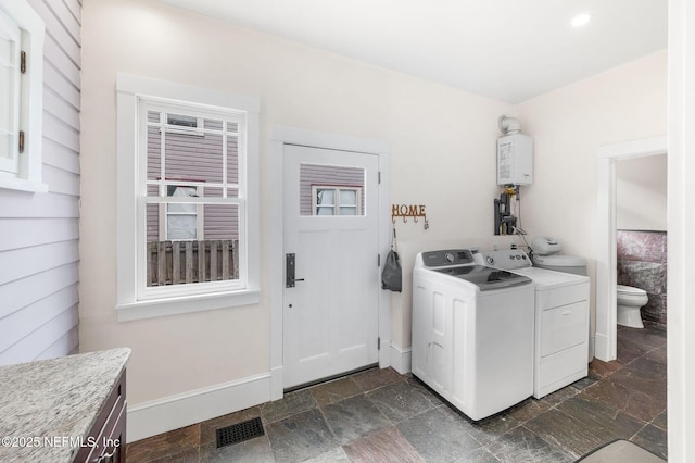 washroom with visible vents, stone finish flooring, water heater, and washing machine and clothes dryer