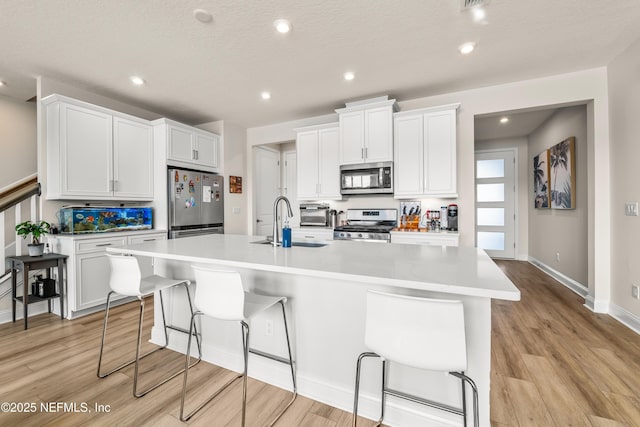 kitchen featuring stainless steel appliances, a sink, a kitchen island with sink, light wood-style floors, and recessed lighting