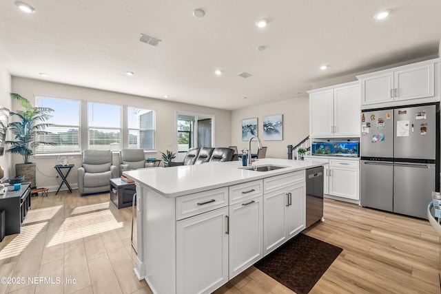kitchen featuring stainless steel appliances, a sink, open floor plan, light wood-type flooring, and recessed lighting