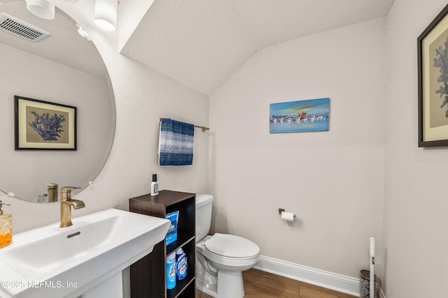 bathroom featuring a sink, toilet, wood finished floors, baseboards, and lofted ceiling