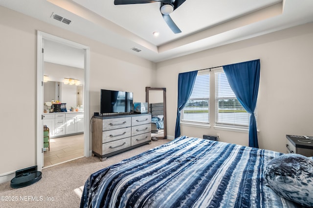 bedroom with carpet floors, a tray ceiling, ensuite bath, ceiling fan, and baseboards