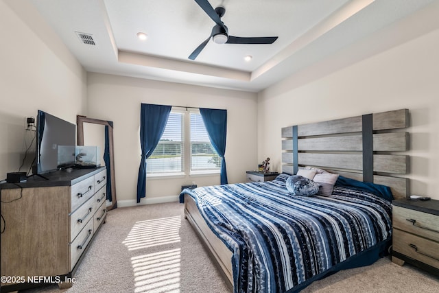 bedroom featuring light carpet, a raised ceiling, baseboards, and a ceiling fan