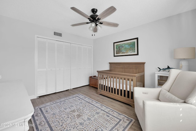 bedroom with wood finished floors, a ceiling fan, a closet, a crib, and visible vents