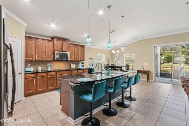 417 Palazzo Cir, Saint Augustine, FL 32092 - kitchen featuring stainless steel microwave, brown cabinetry, crown molding, a kitchen bar, and vaulted ceiling