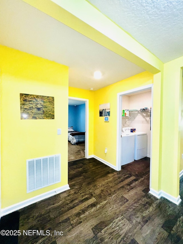 hall with a textured ceiling, visible vents, baseboards, separate washer and dryer, and wood finished floors