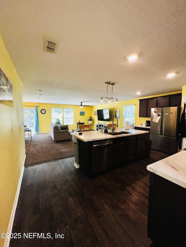 kitchen featuring a sink, dark wood-style flooring, stainless steel appliances, light countertops, and open floor plan