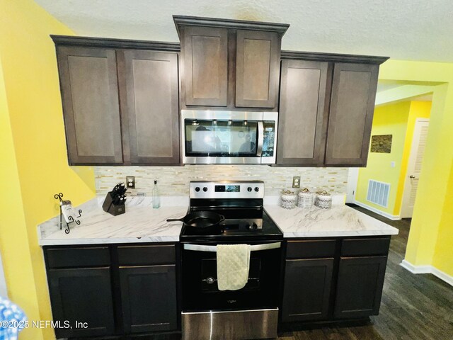 kitchen with dark wood finished floors, visible vents, stainless steel appliances, and decorative backsplash