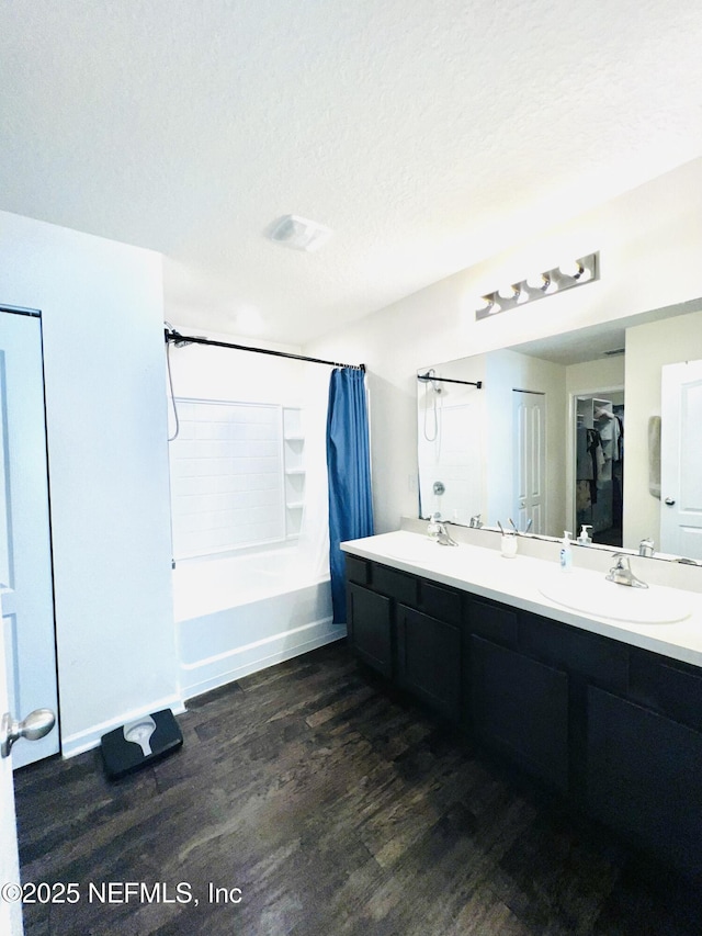 bathroom with a textured ceiling, a sink, double vanity, shower / tub combo with curtain, and wood finished floors