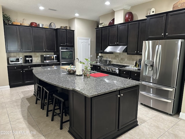 kitchen featuring dark cabinetry, stainless steel appliances, and under cabinet range hood