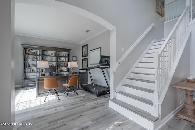 interior space featuring wood finished floors, crown molding, baseboards, and arched walkways