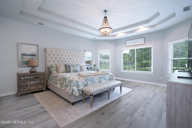 bedroom with light wood-style flooring, multiple windows, visible vents, a raised ceiling, and a notable chandelier