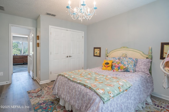 bedroom featuring visible vents, wood finished floors, a notable chandelier, and a closet