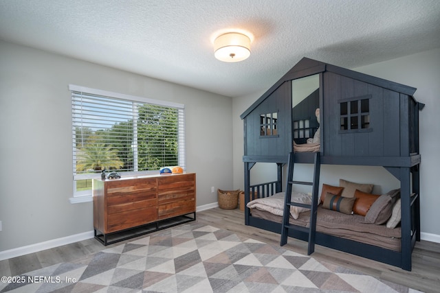 bedroom with light wood finished floors, a textured ceiling, and baseboards
