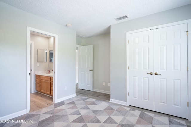 unfurnished bedroom featuring light wood-style flooring, a closet, baseboards, visible vents, and a textured ceiling