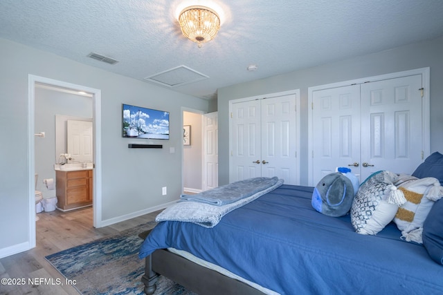 bedroom featuring wood finished floors, multiple closets, baseboards, visible vents, and a textured ceiling