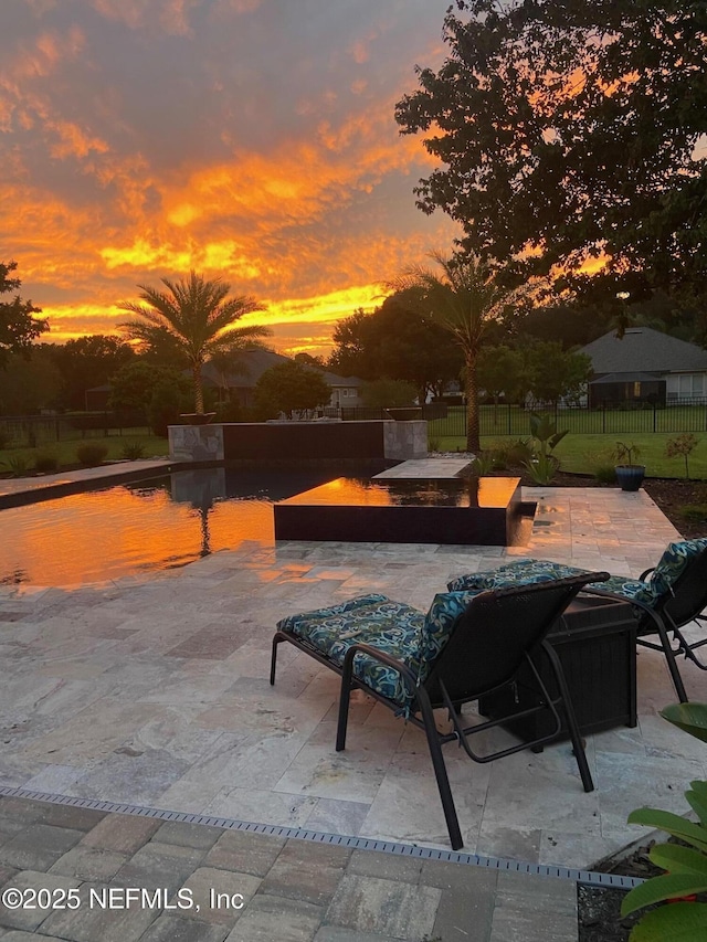 patio terrace at dusk featuring fence and an outdoor pool